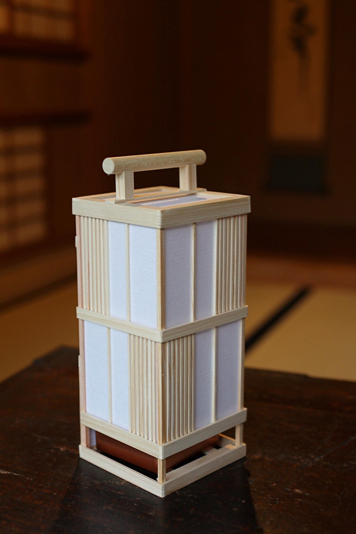 A wooden lantern with a handle, sitting on a dark surface.