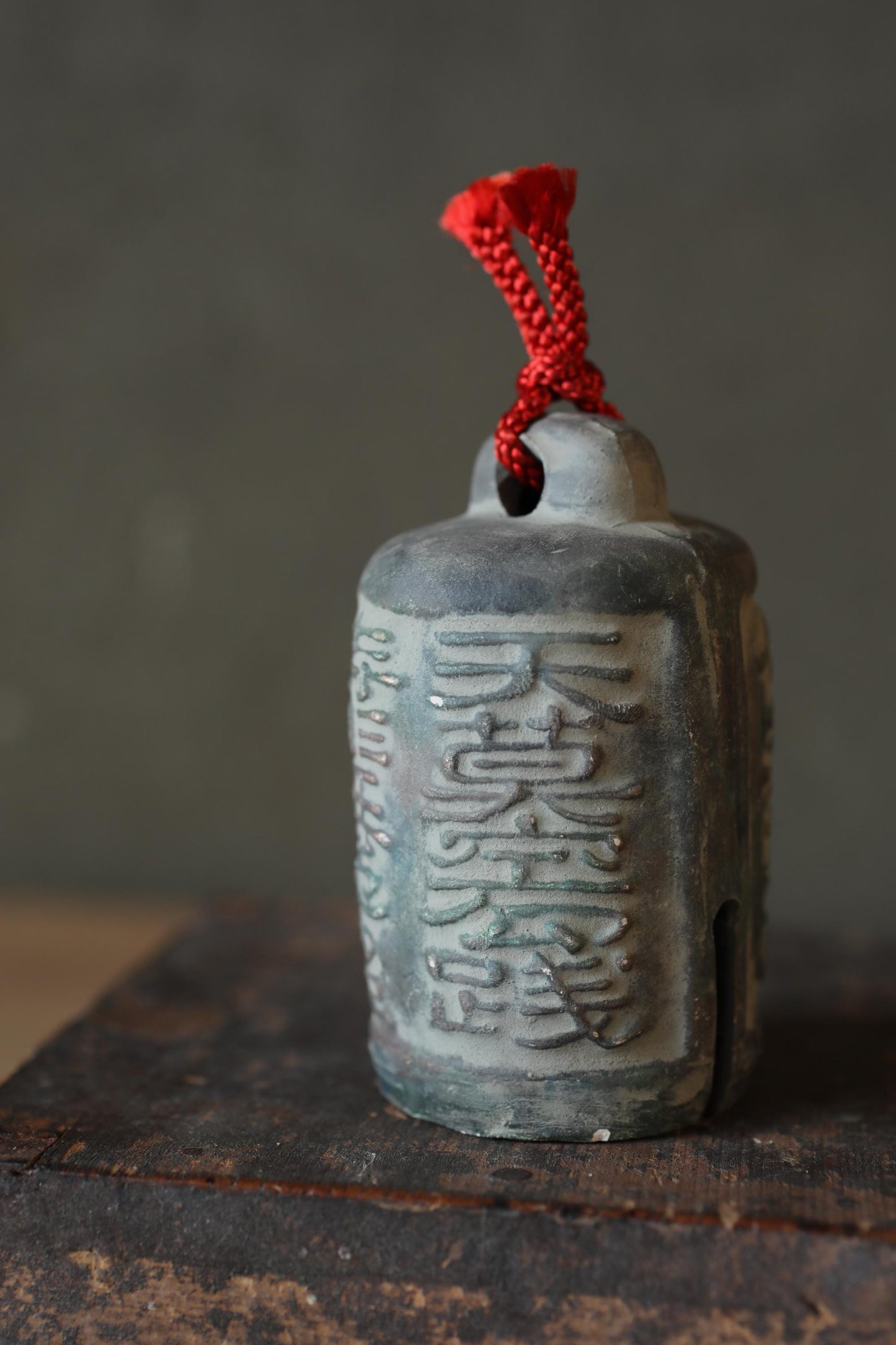 A close-up image of a metal bell with a red string attached to it, resting on a wooden surface.