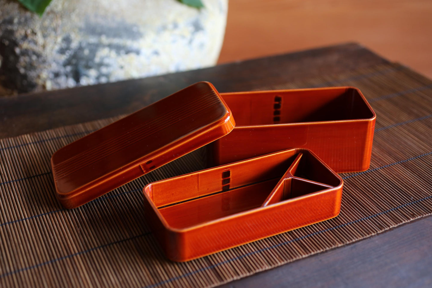 two orange bento box containers placed on a bamboo placemat.