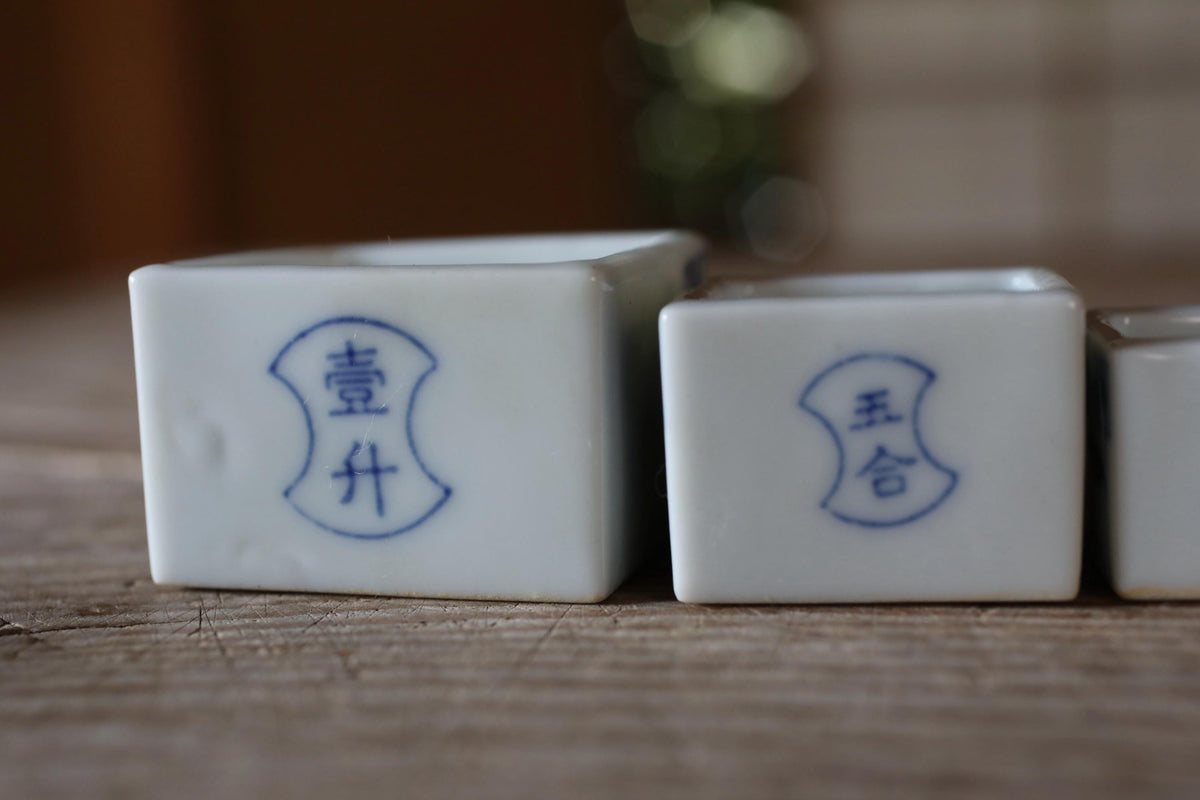 two white ceramic containers with blue Chinese characters on them, placed on a wooden surface.