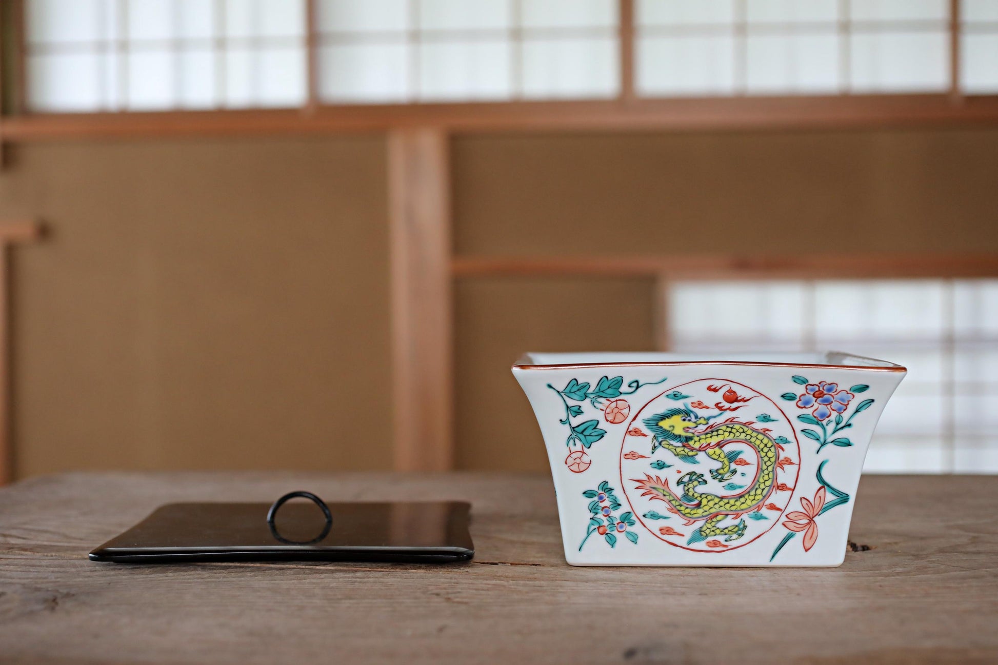 a white ceramic bowl with a dragon design, placed on a wooden surface next to a black object, possibly a ring or a small decorative item.