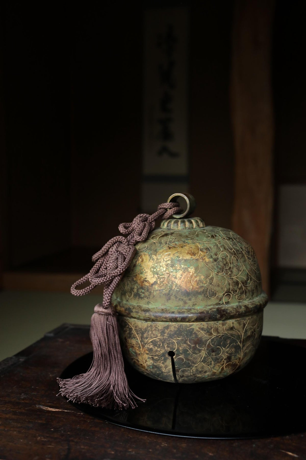 A decorative bell with a tassel and a wooden base, placed on a dark surface.