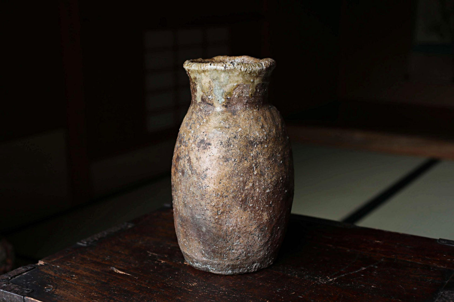 An old, weathered vase sits on a wooden surface, its surface showing signs of age and use.