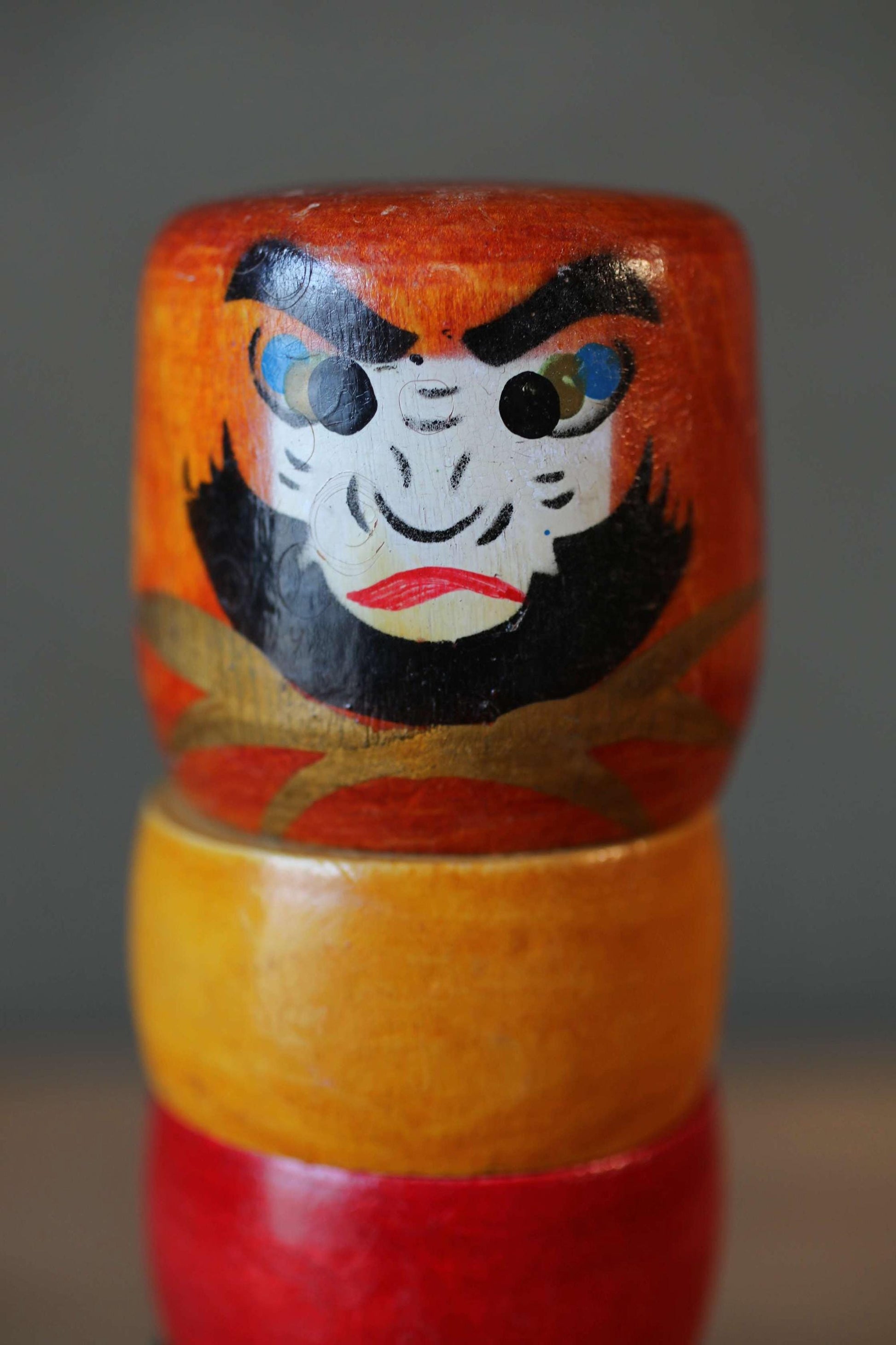 A colorful wooden doll with a face painted on it, sitting on top of two stacked wooden dolls.