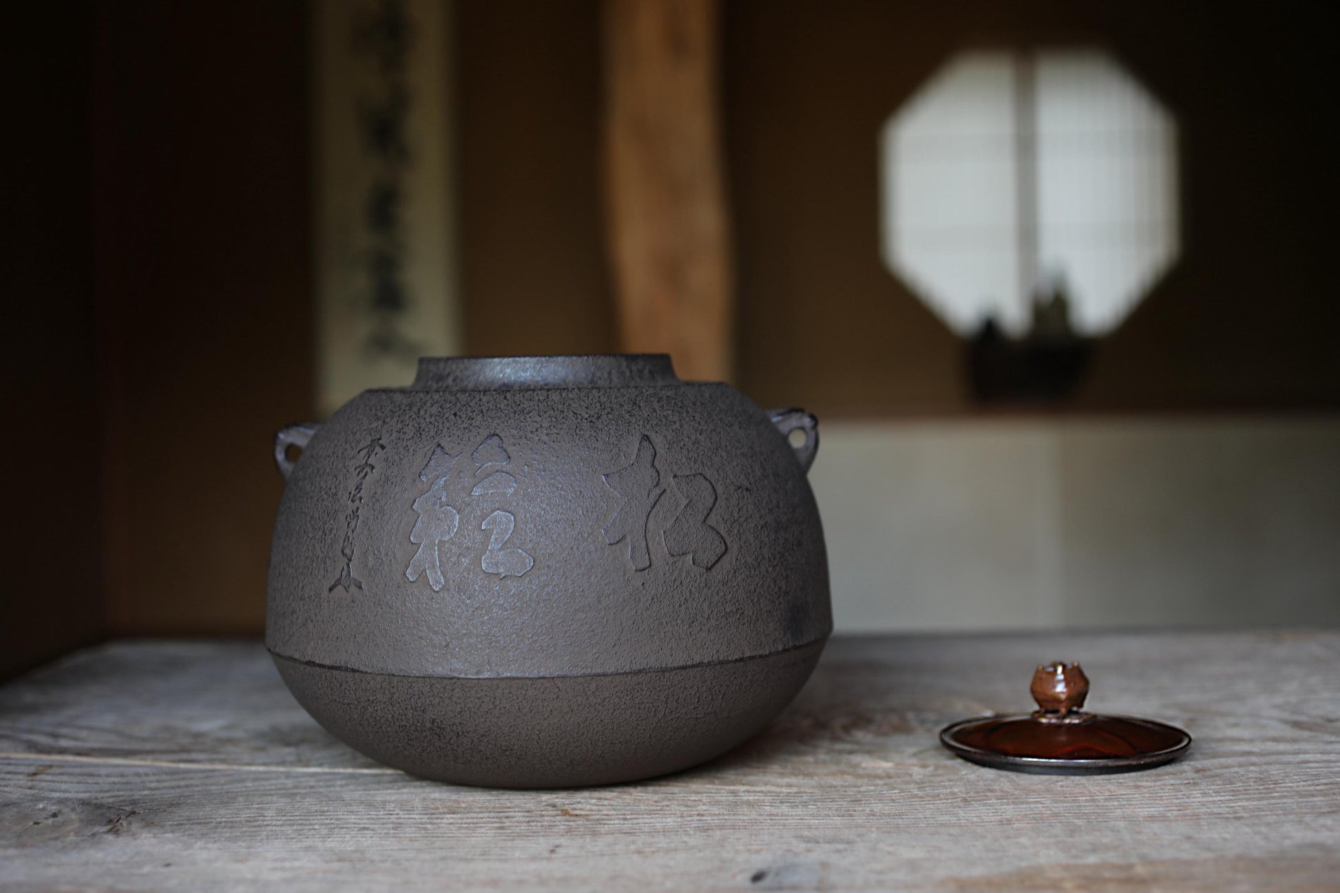 A black ceramic tea pot with Chinese characters on it, placed on a wooden surface, with a small lid next to it.