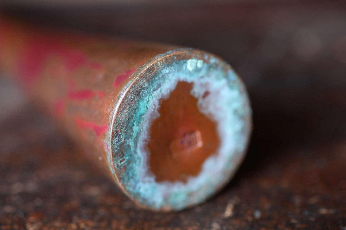 A close-up view of a rusted metal pipe with a hole in the center, revealing a copper-colored interior.