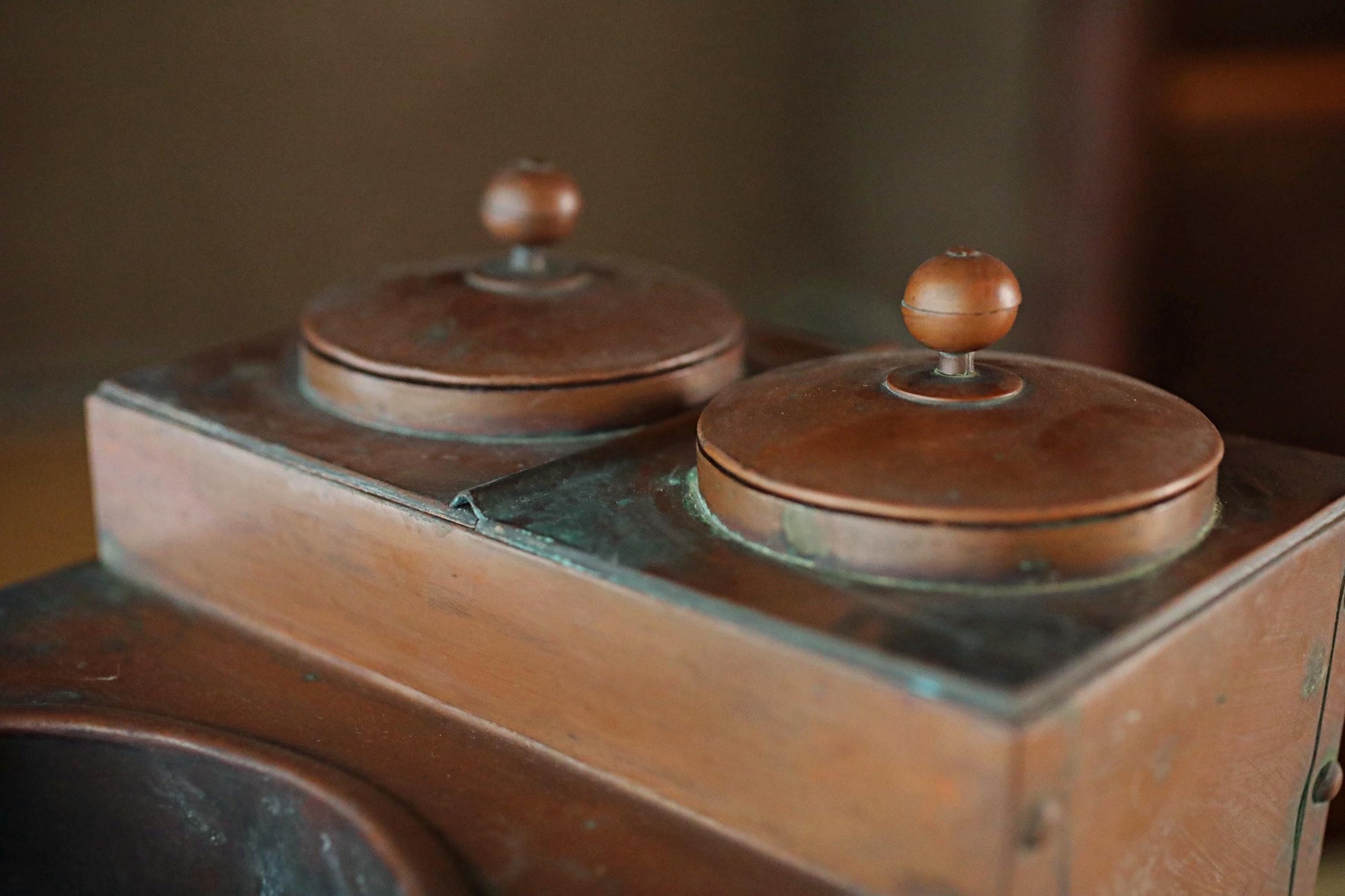 a close-up view of a copper-colored metal object, possibly a container or a piece of furniture, with two round tops and a rectangular base.