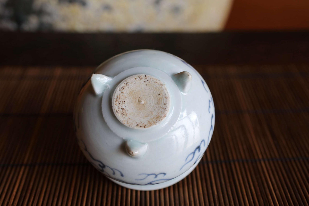 A white ceramic bowl with blue designs sits on a bamboo mat.