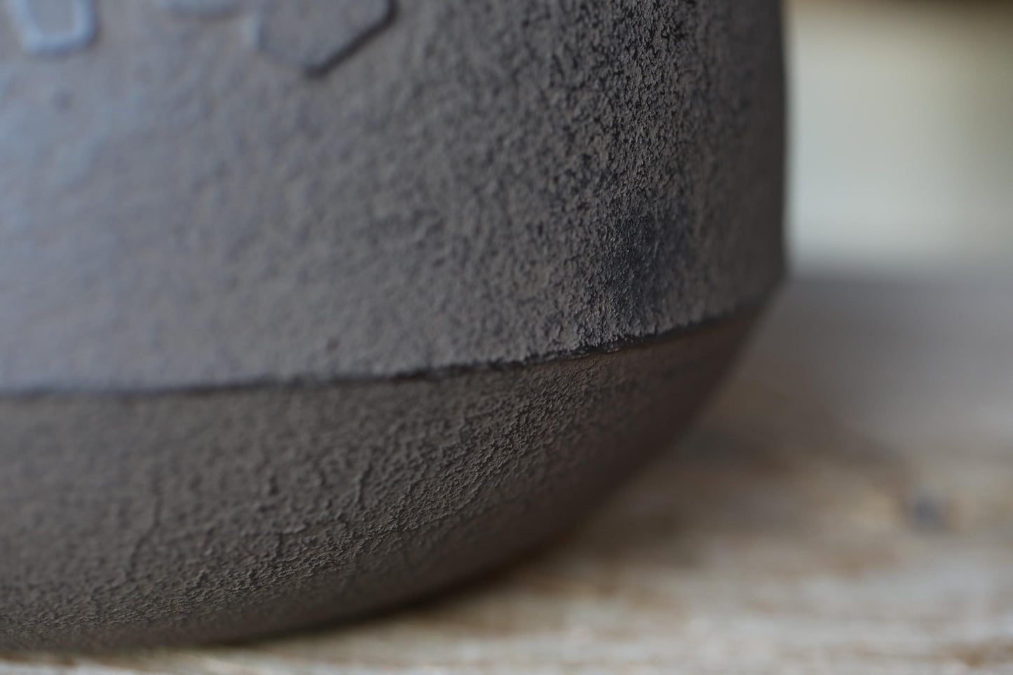 A close-up view of a textured, dark gray surface, possibly a ceramic or metal object, with a blurred background.