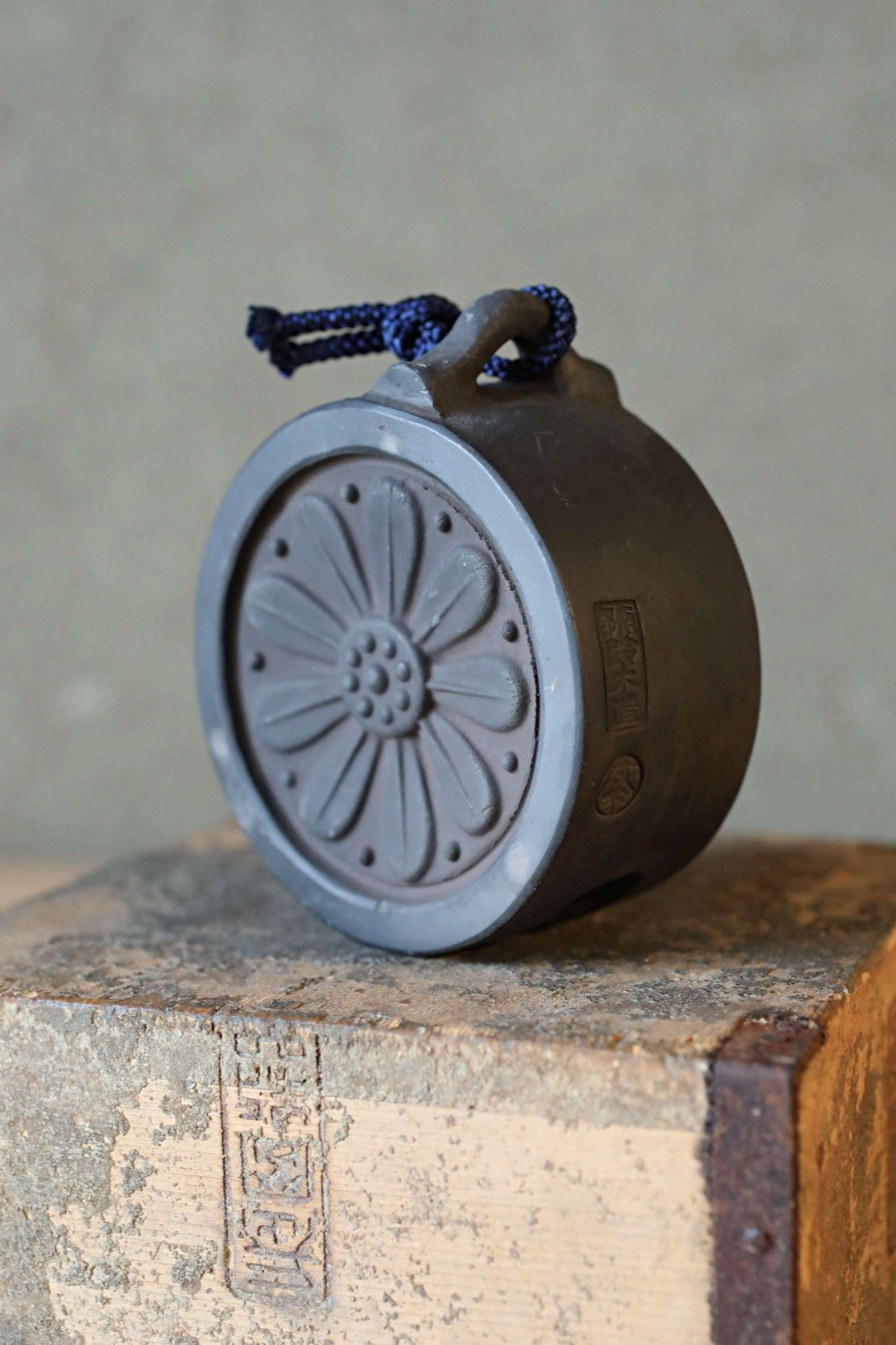 A black ceramic object with a blue string attached to it, sitting on a wooden surface.