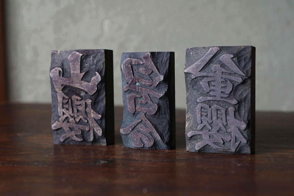 Three dark-colored rectangular blocks with intricate carved designs, likely made of wood or stone, arranged on a wooden surface.