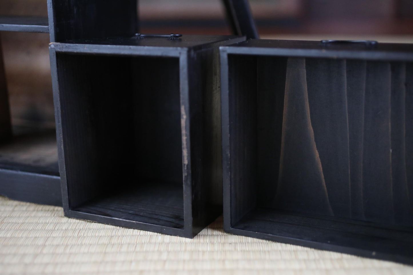 two black wooden boxes with empty interiors, placed side by side on a woven mat.