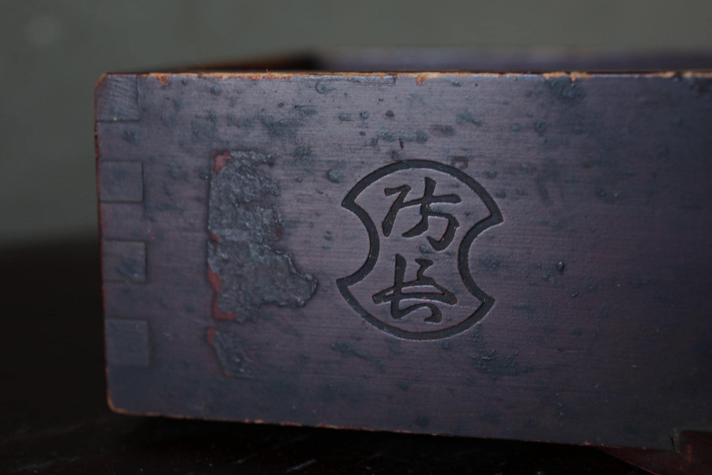 a close-up view of a dark wooden surface with a carved symbol or logo, possibly a name or brand mark, in the center.
