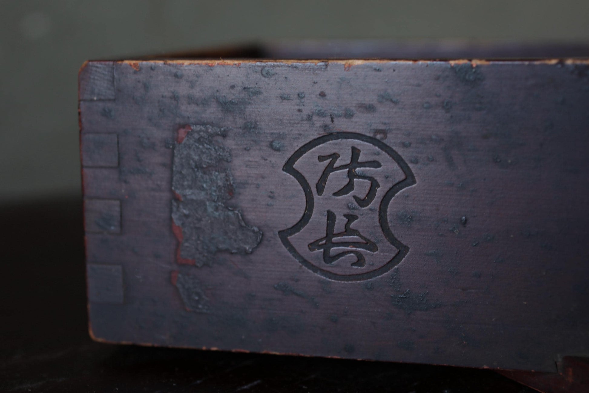a close-up view of a dark wooden surface with a carved symbol or logo, possibly a name or brand mark, in the center.