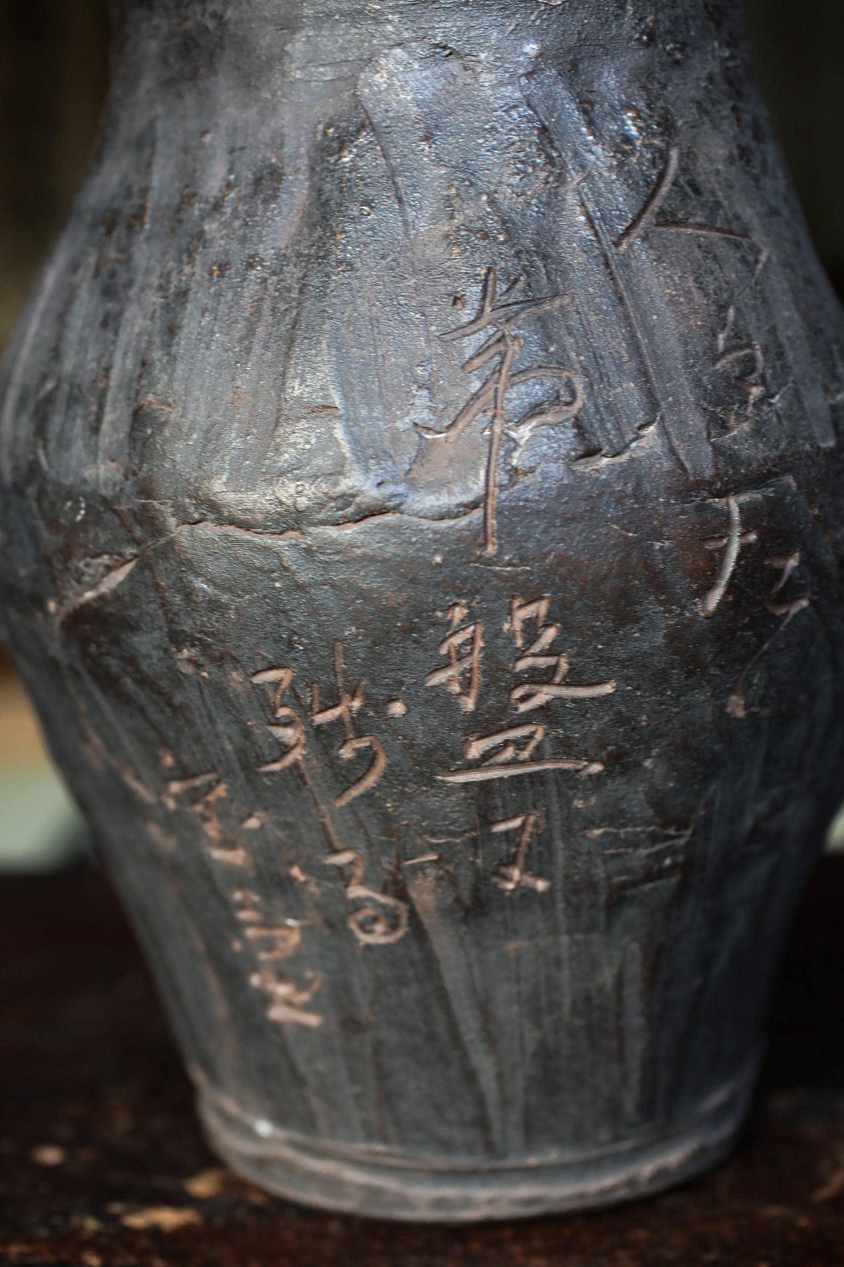 a close-up view of a dark-colored vase with intricate carvings and markings in an Asian script.