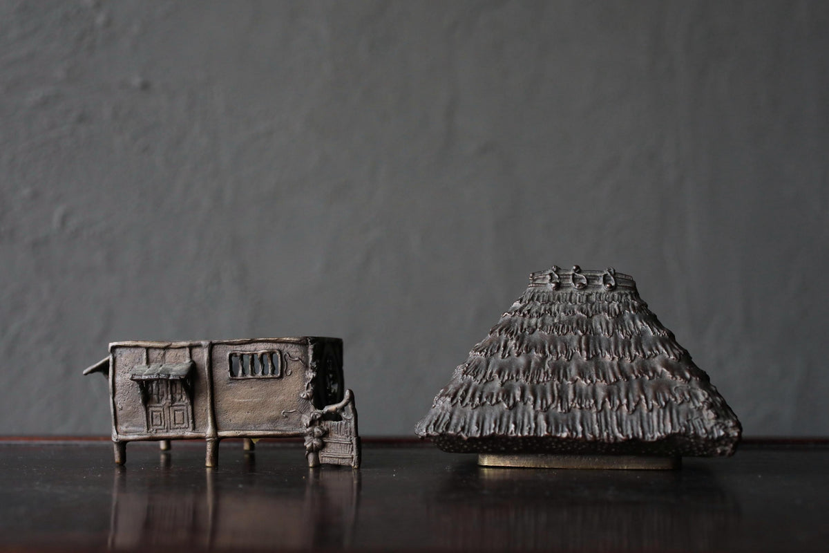two small, intricately designed metal figurines placed on a dark surface against a gray background.