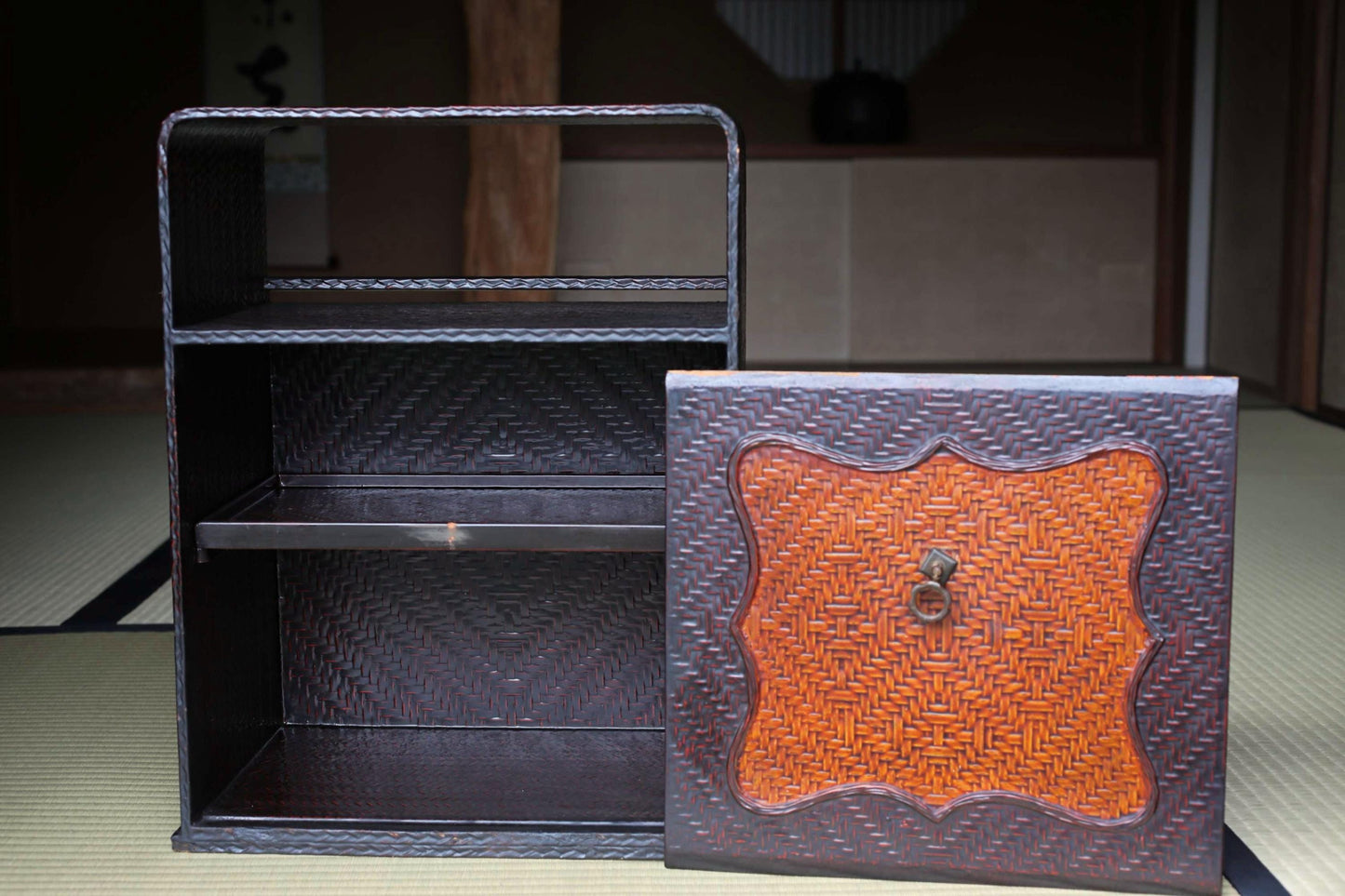 a black woven shelf with a decorative orange design on the front, placed on a tatami mat.