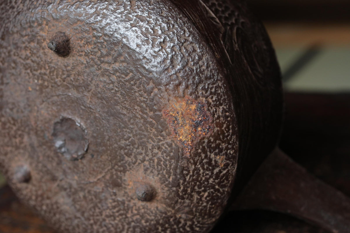 A close-up view of a rusted metal object, possibly a piece of furniture or a decorative item, with a textured surface and a small, circular hole in the center.