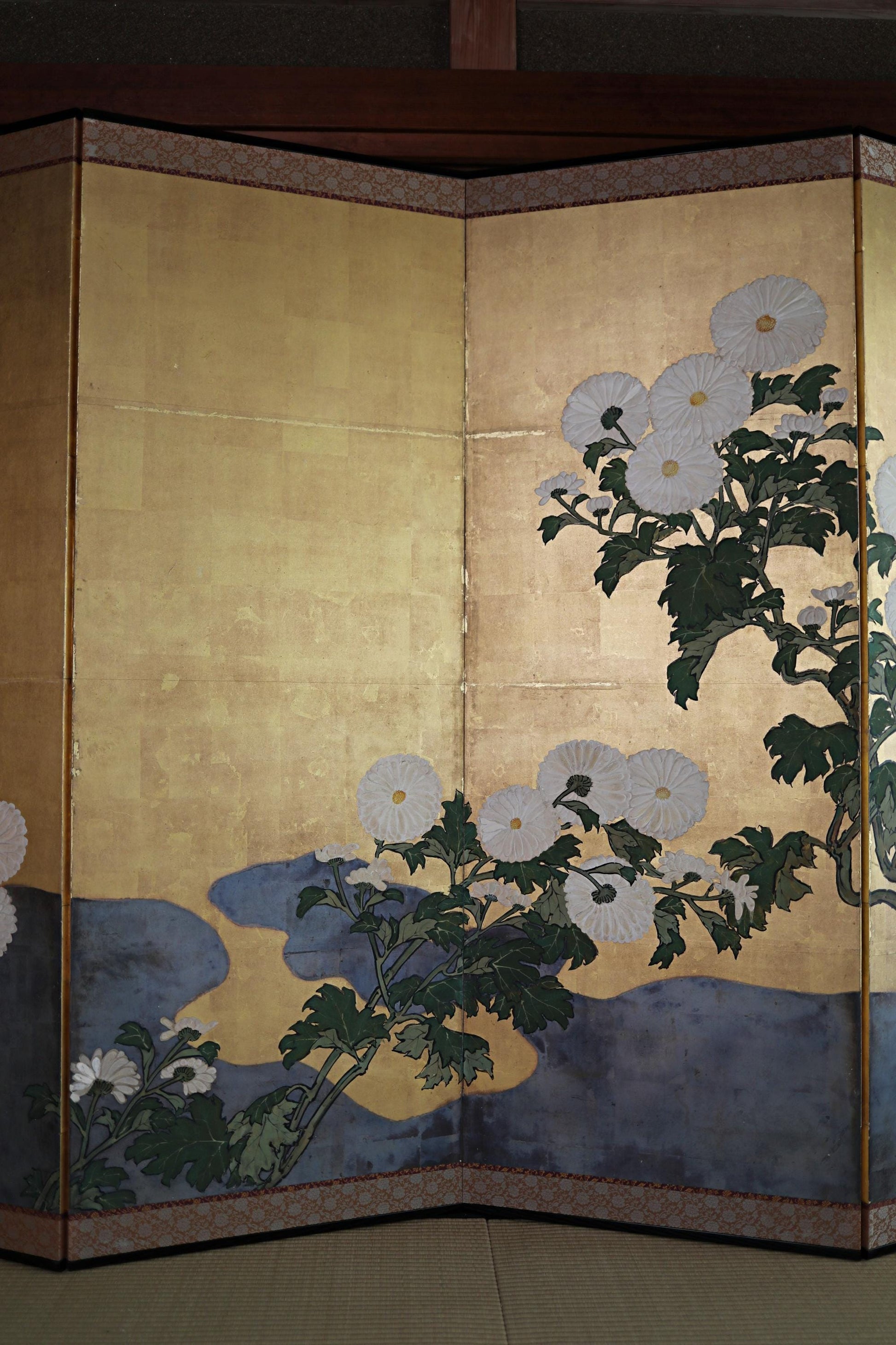 a large, intricately designed screen with a floral motif. The screen is composed of multiple panels, each showcasing a different flower arrangement. The flowers are white and green, and the overall design is visually striking and detailed.