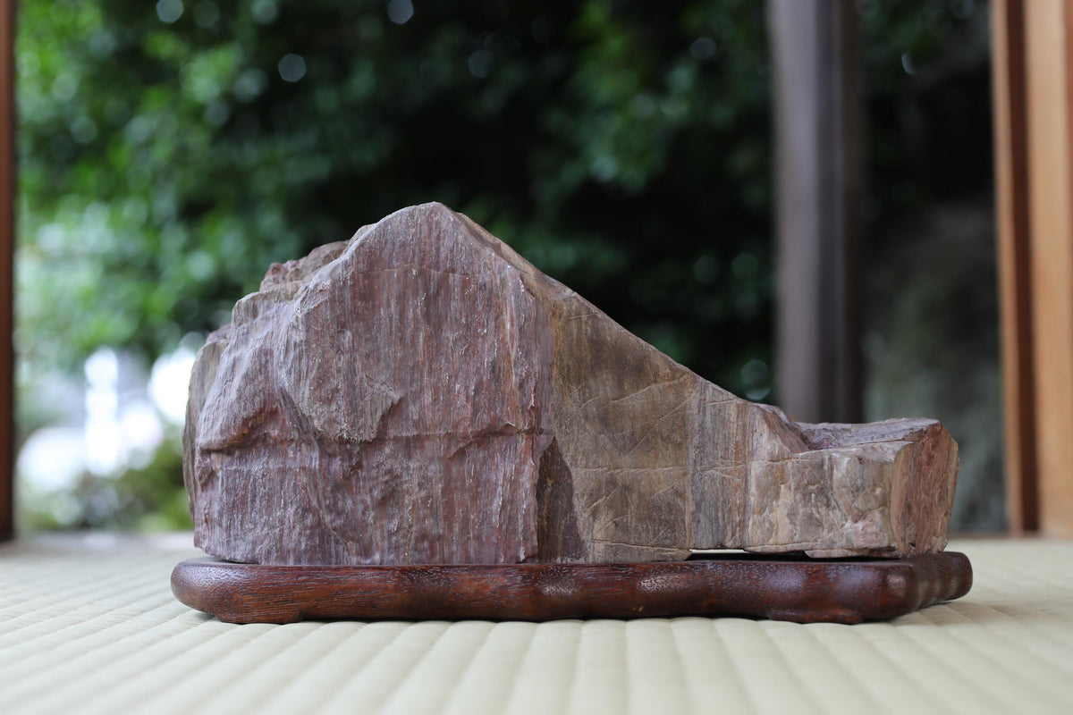 A large, irregularly shaped rock sits on a wooden base, placed on a wooden surface.