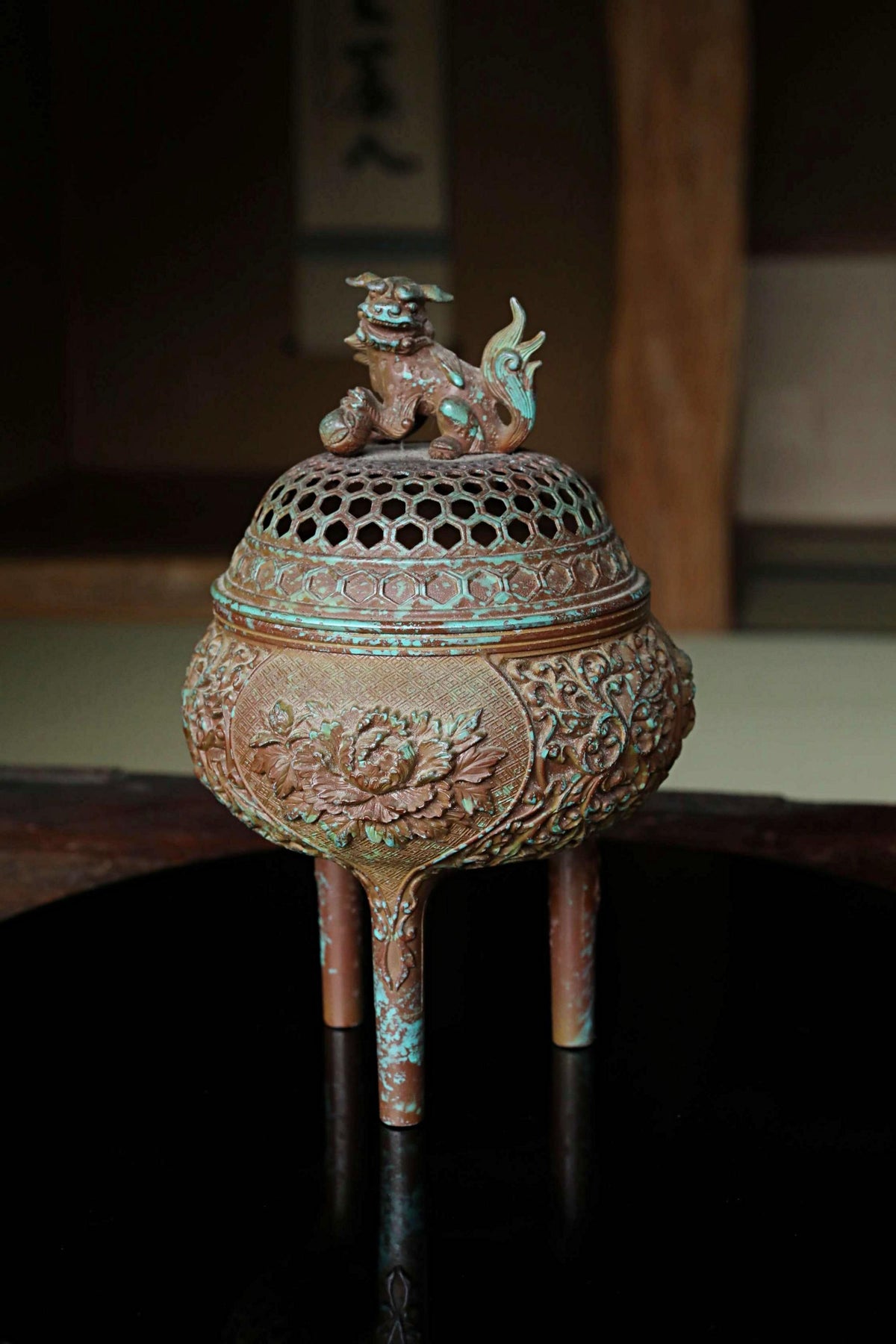 An ornate bronze incense burner with a dragon design on top, placed on a dark surface.