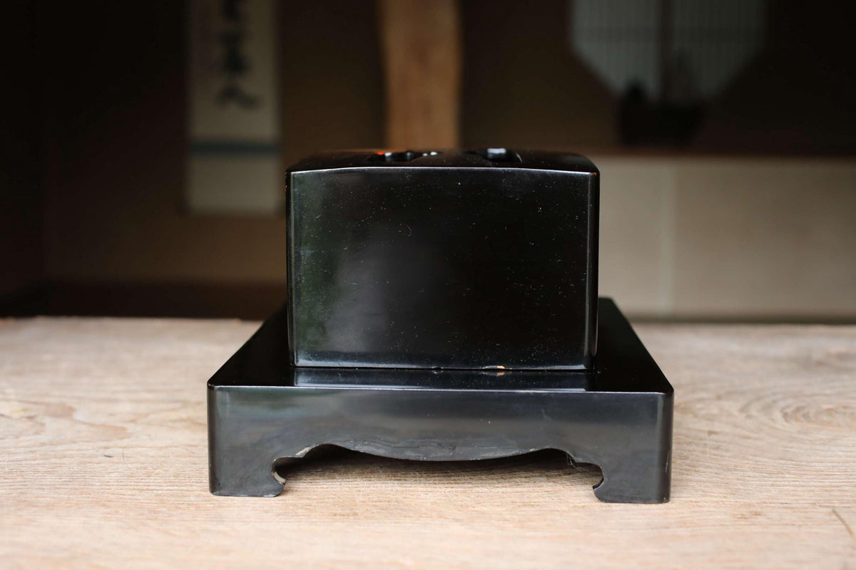 A black rectangular object is sitting on a wooden surface, with a blurred background.