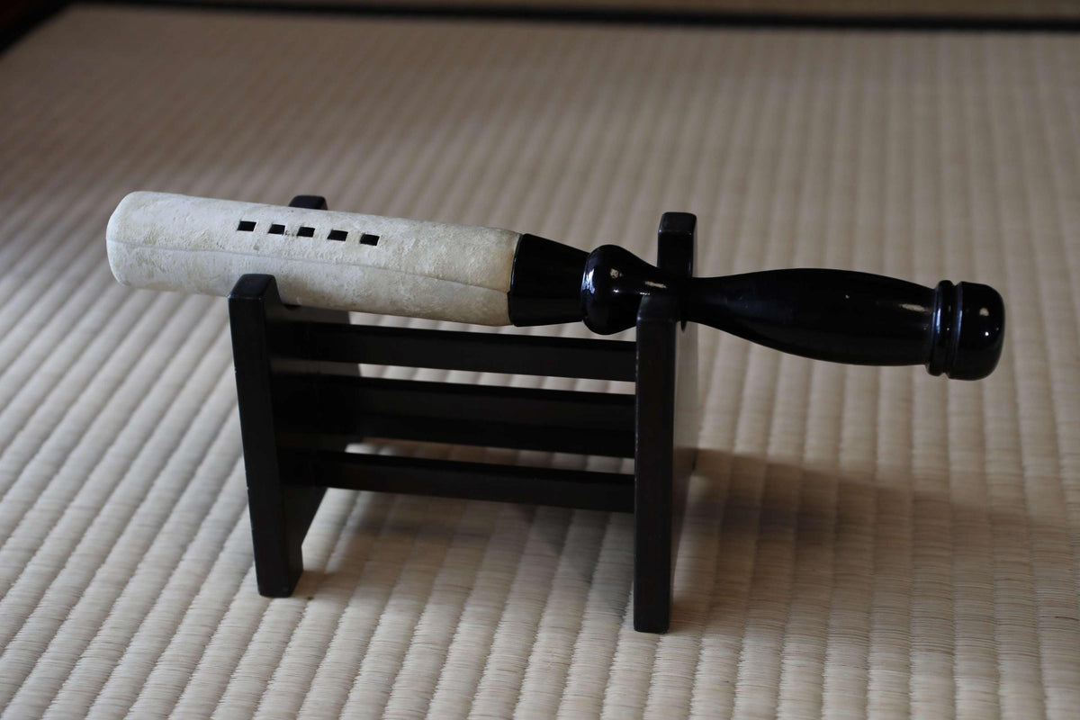 A wooden stand holding a white and black object, possibly a musical instrument or tool, on a woven mat.