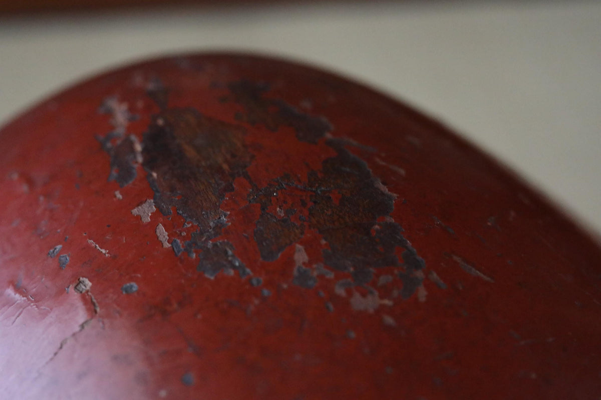 A close-up view of a red, weathered metal surface with a dark, chipped area in the center.