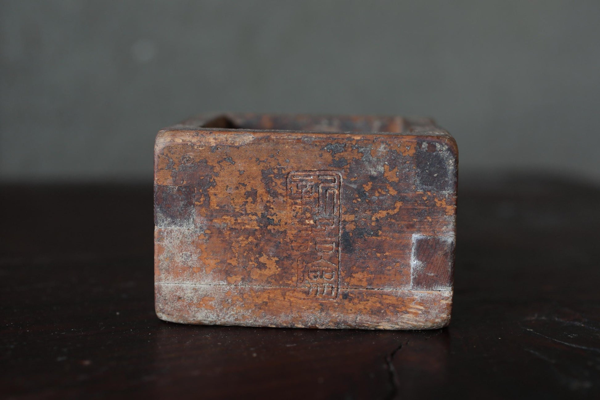 An old, rusted metal object with a weathered, distressed appearance sits on a dark surface.