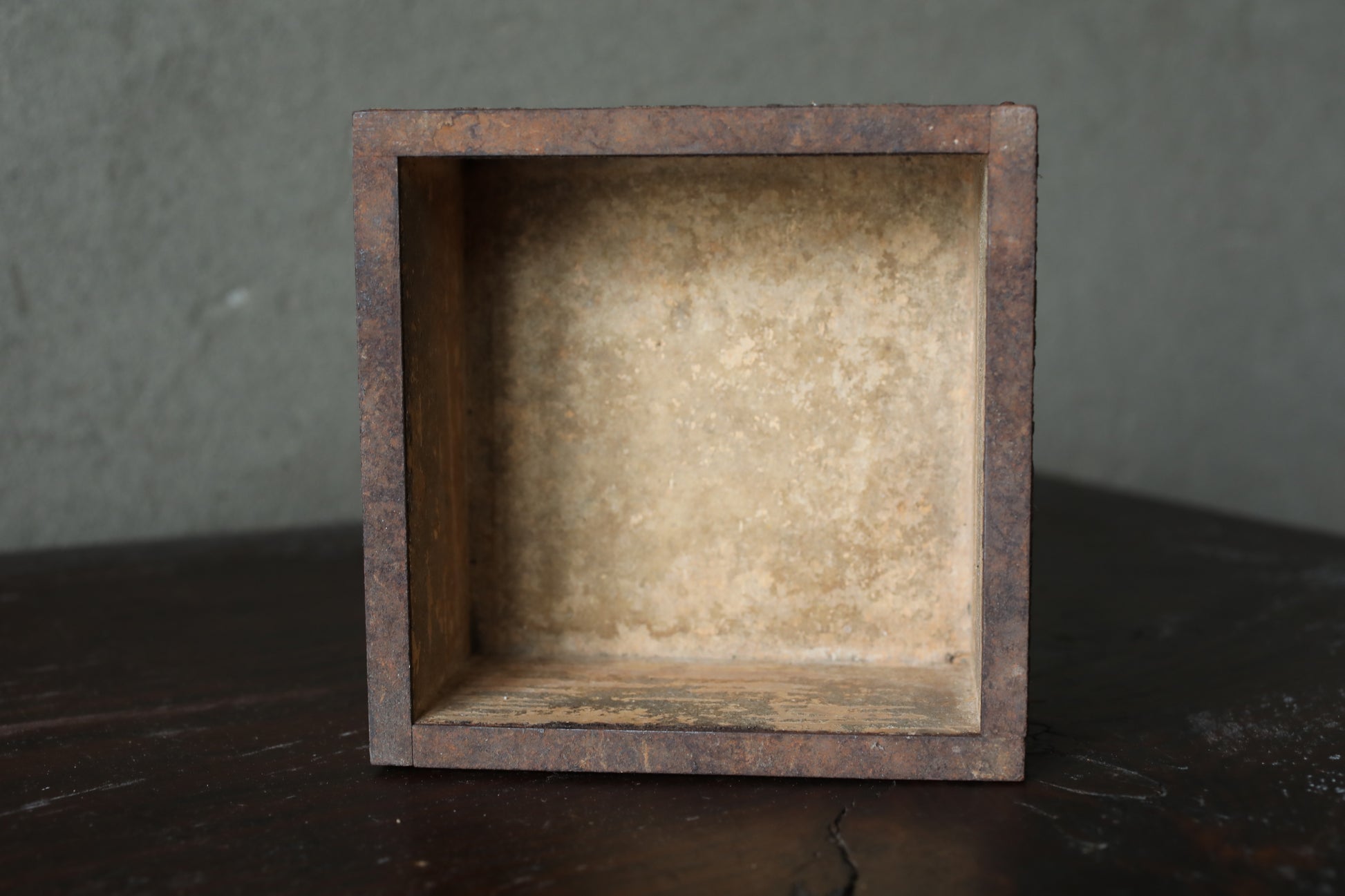 a rustic, weathered wooden box with a rough, textured surface, sitting on a dark surface.
