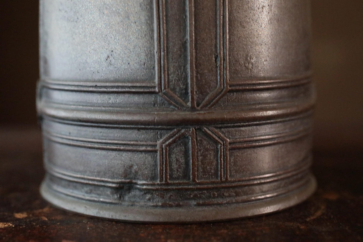 A close-up view of a metal object, possibly a vase or container, with a textured surface and a decorative pattern.