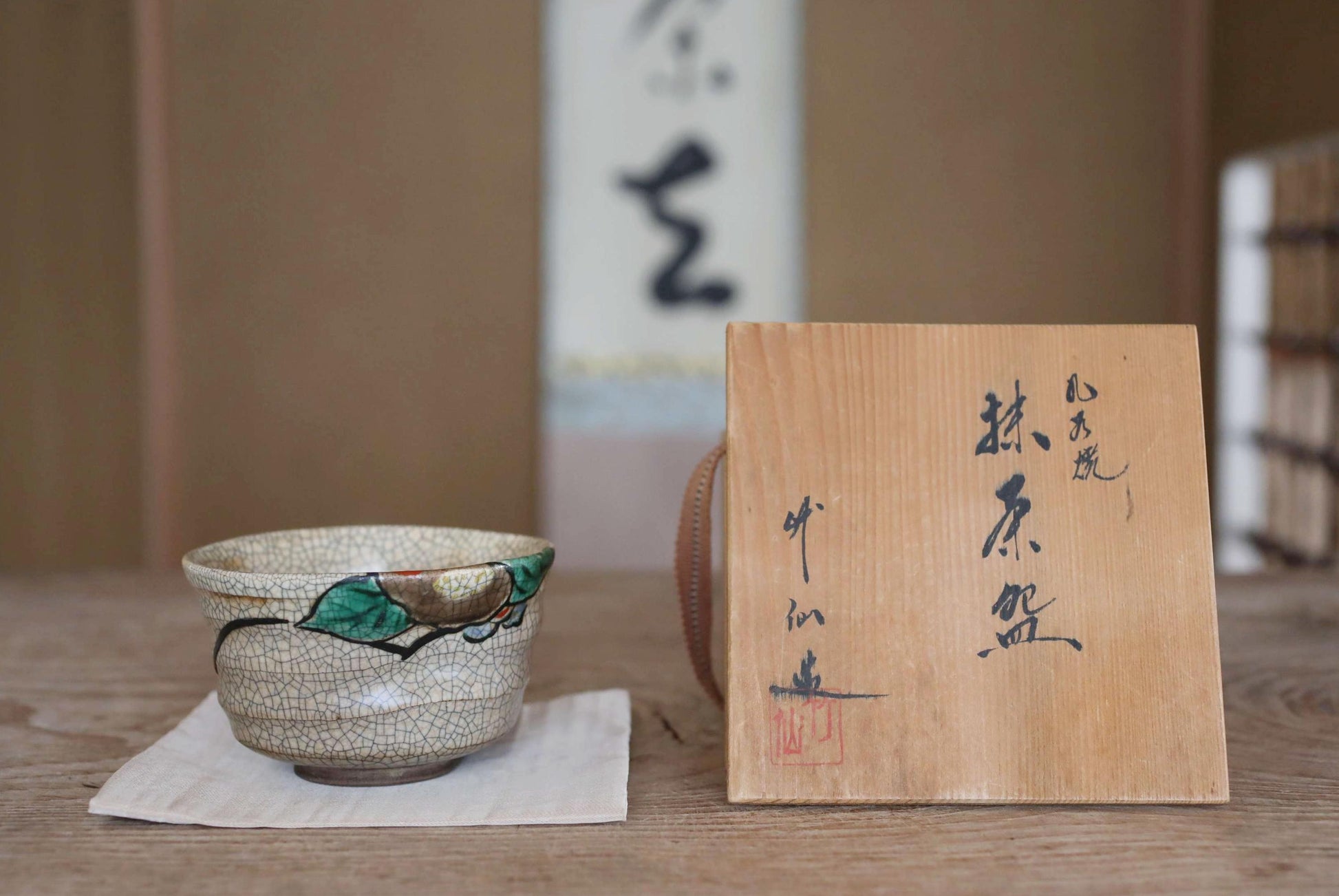 a ceramic bowl with a leaf design and a wooden sign with Japanese characters on a wooden surface.