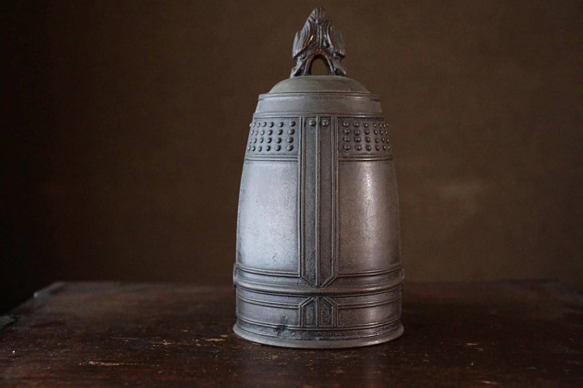 A metal bell with a decorative design on its surface, sitting on a wooden surface.