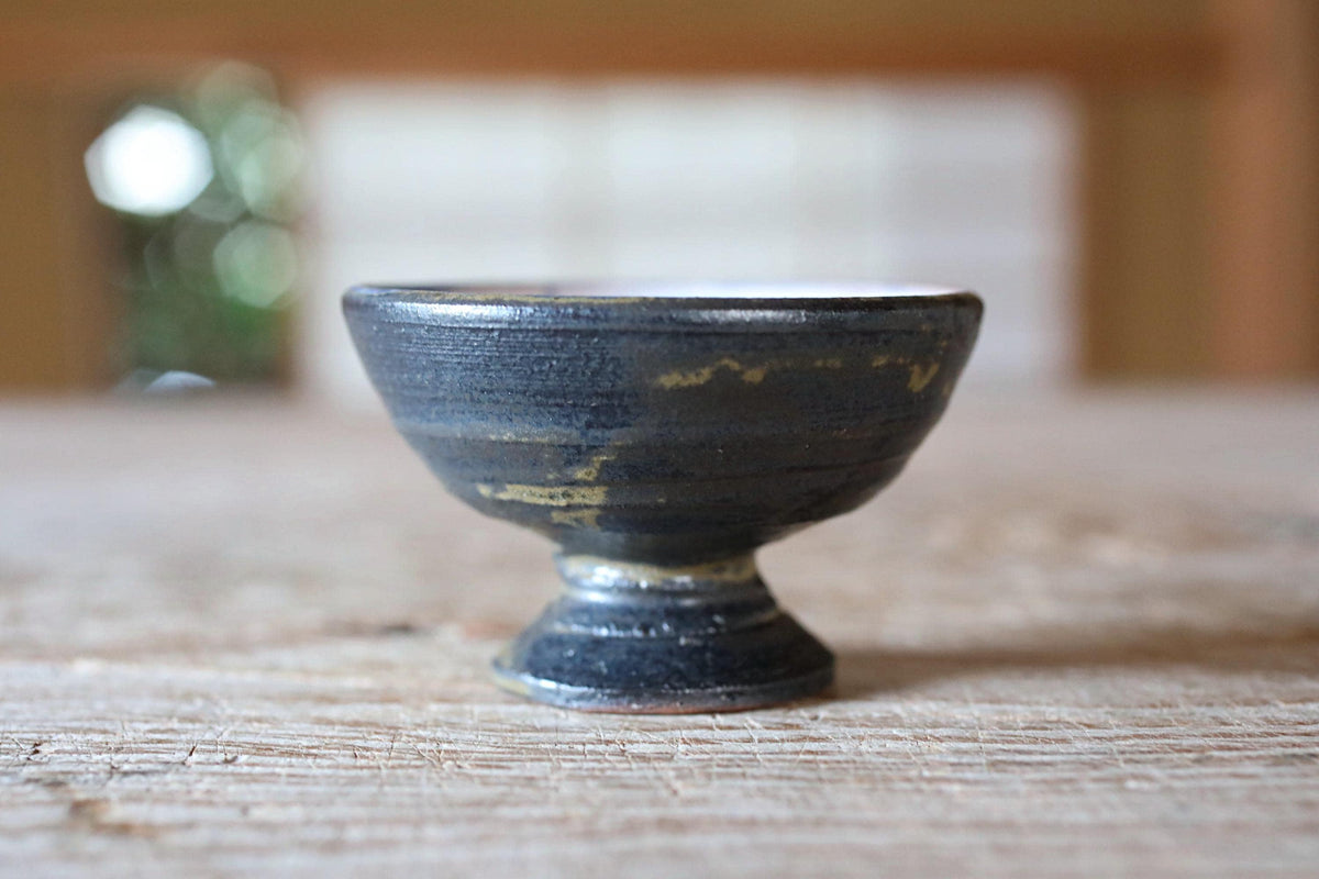 A small, black ceramic bowl with a textured surface sits on a wooden surface.
