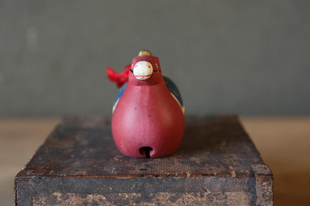 A red bird figurine with a red ribbon around its neck is sitting on a wooden surface.