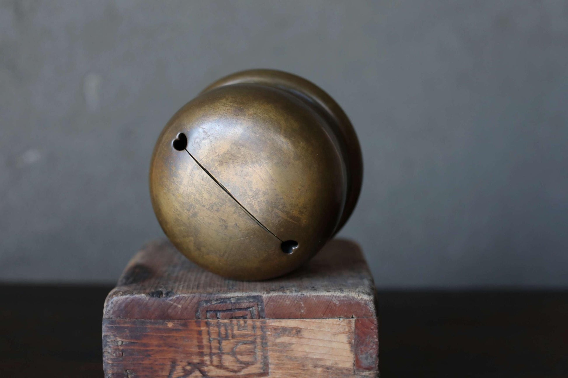 A brass bell with a hole in the center is placed on a wooden block against a gray background.