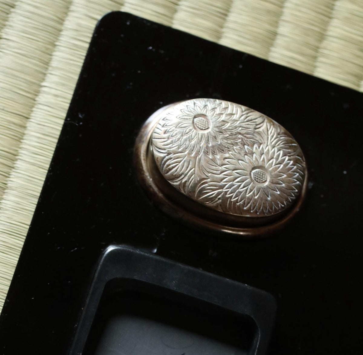 a close-up view of a decorative metal object, possibly a piece of jewelry or a small sculpture, resting on a black surface.