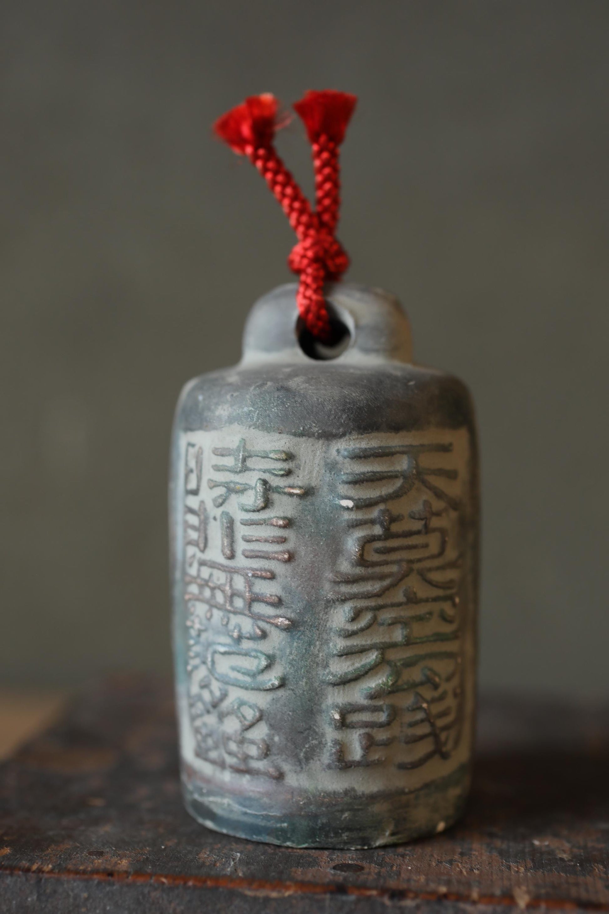 A close-up image of a ceramic object with Chinese characters on it, featuring a red string or cord attached to the top.