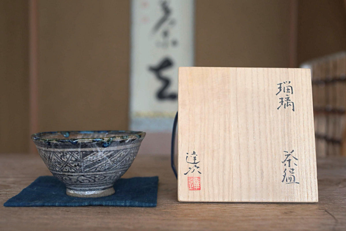 a wooden box with Japanese characters on it, placed next to a decorative bowl on a wooden surface.