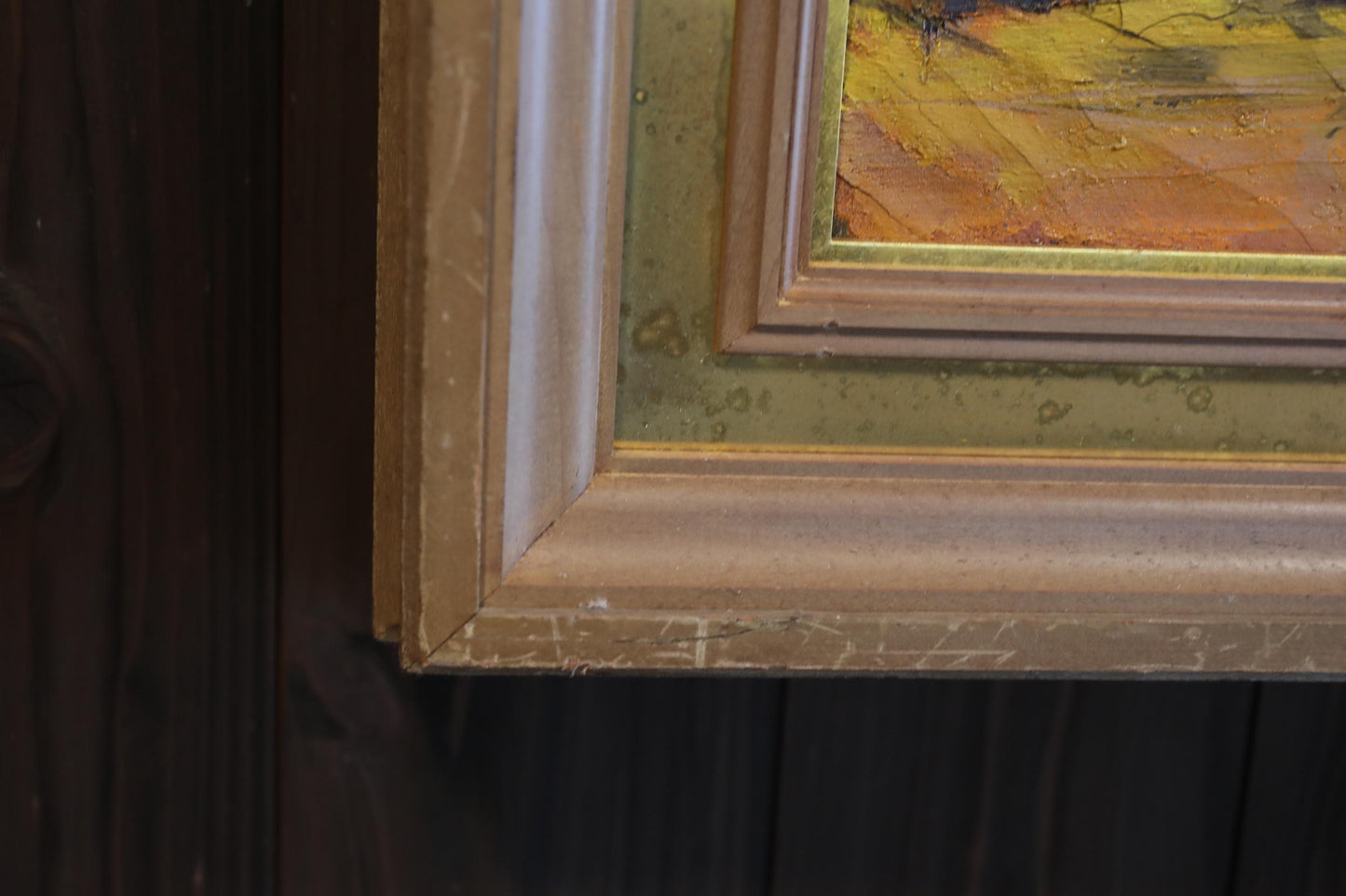 a close-up view of a wooden frame with a painting inside it, set against a dark wooden background.