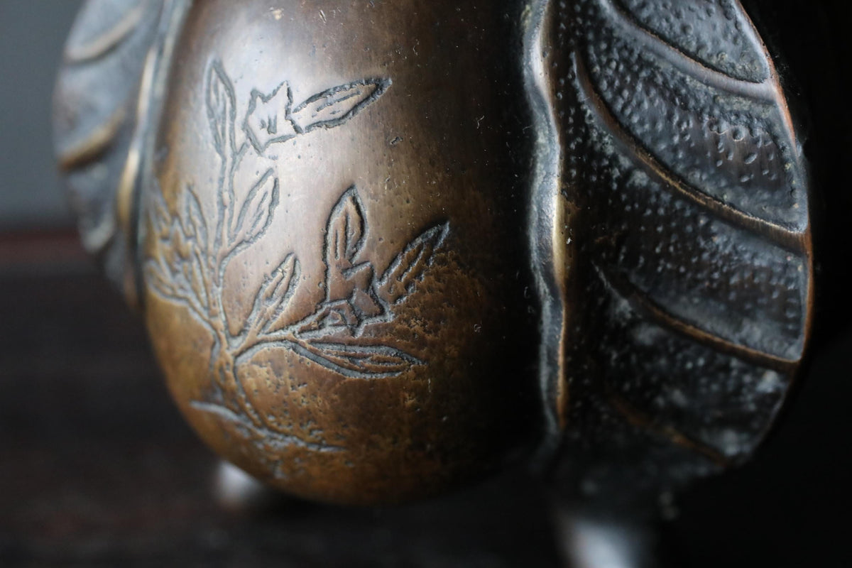 A close-up view of a decorative metal object, possibly a vase or container, with intricate engraved designs on its surface.