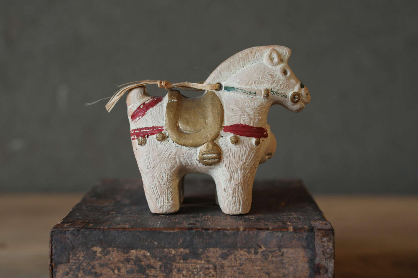 A small white ceramic figurine of a horse, with a saddle and decorative elements, is displayed on a wooden surface.