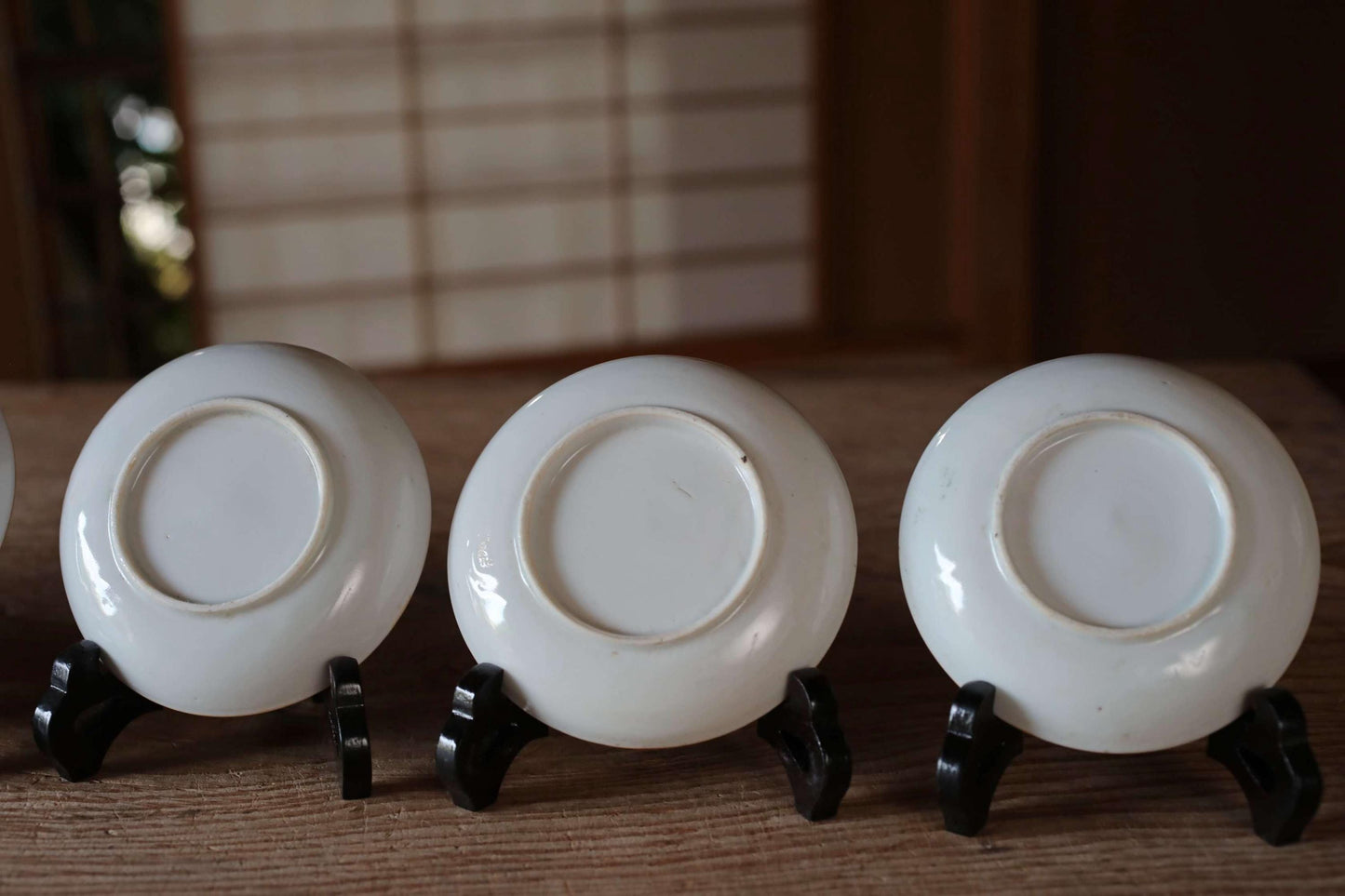 Three white ceramic plates or bowls are arranged in a row on a wooden surface, each resting on a black stand.
