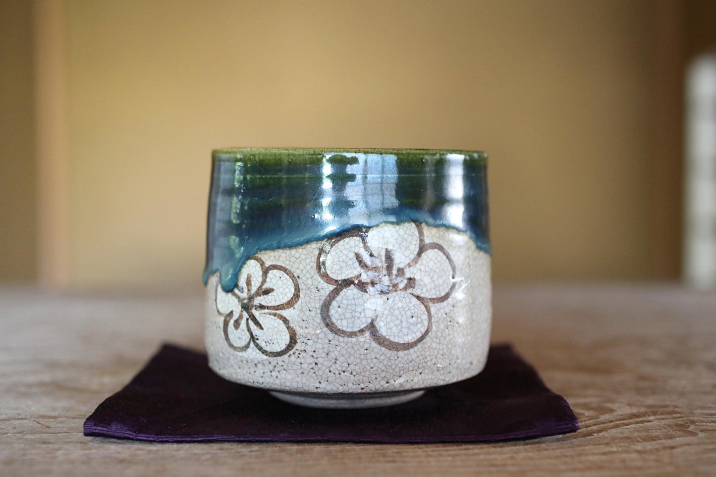 A ceramic mug with a floral design sits on a purple cloth on a wooden surface.