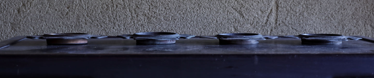 four metal objects with circular shapes, arranged in a row on a dark surface.