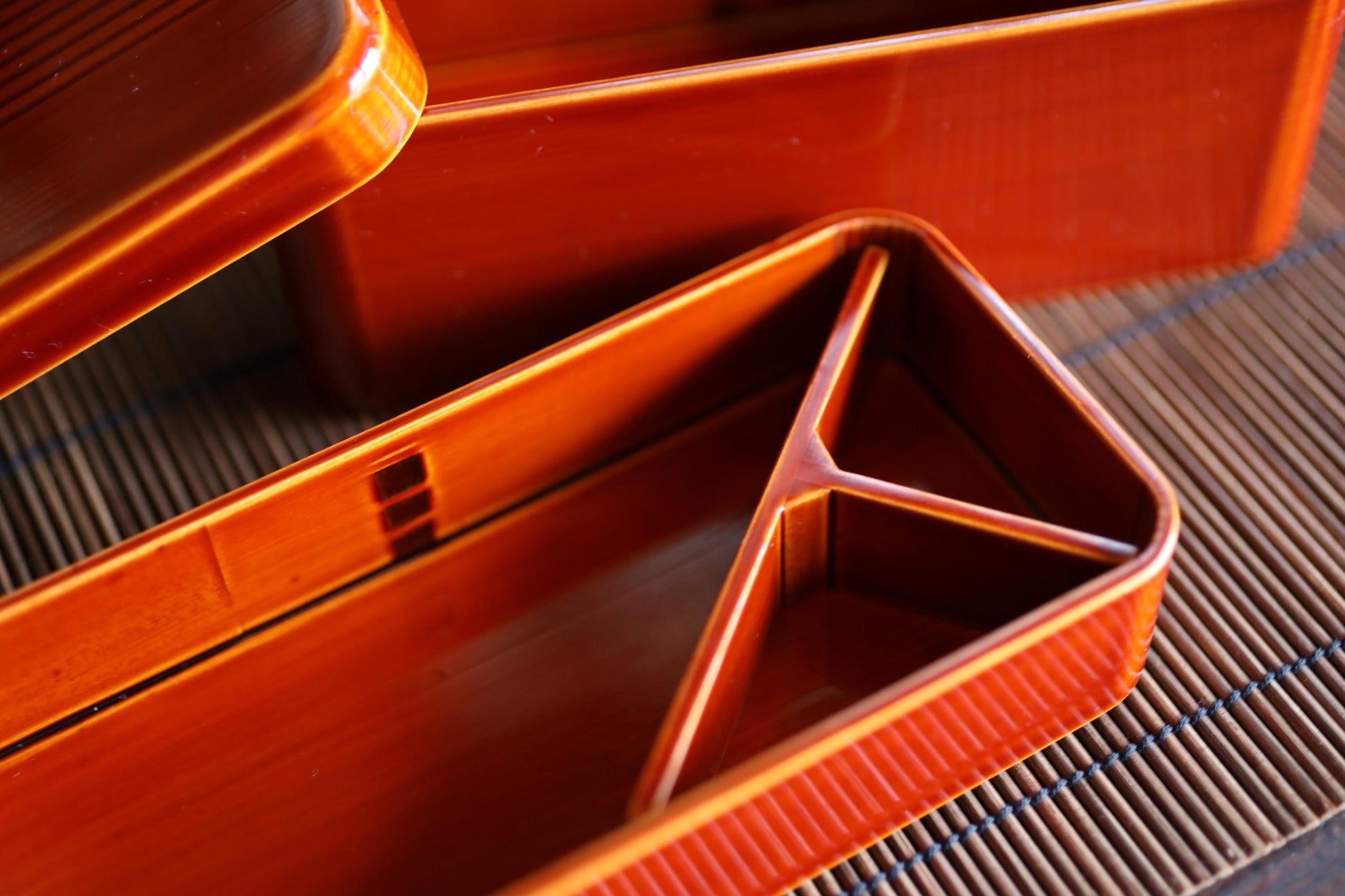 a close-up view of a red bento box with a triangular compartment, resting on a bamboo mat.