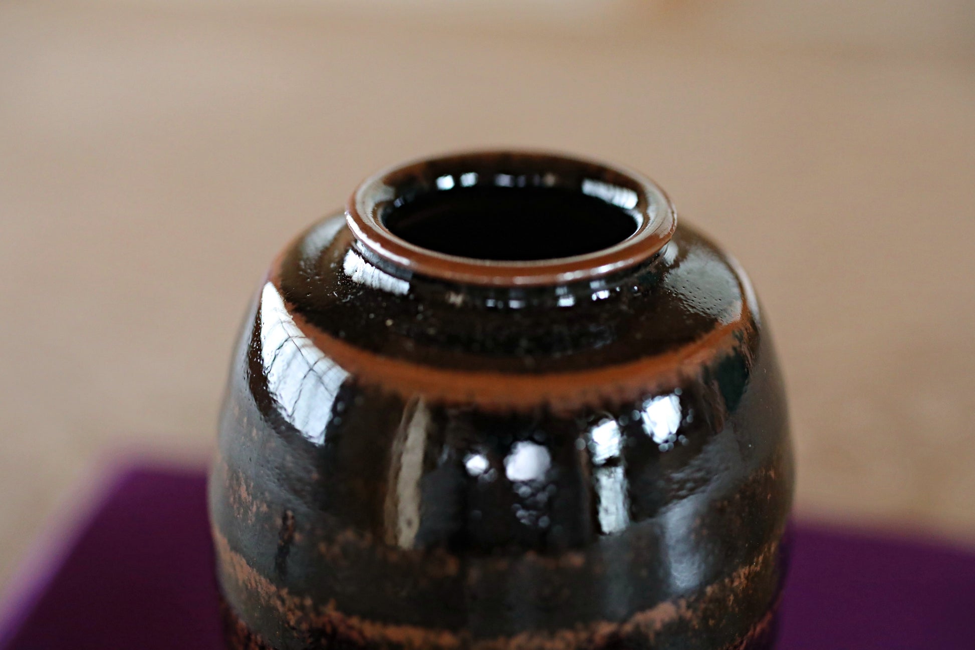A close-up view of a dark brown ceramic vase with a shiny, reflective surface.