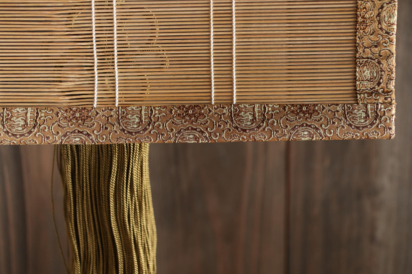a close-up view of a decorative bamboo shade with a tassel hanging from the bottom. The bamboo shade has a patterned border and appears to be made of wood.