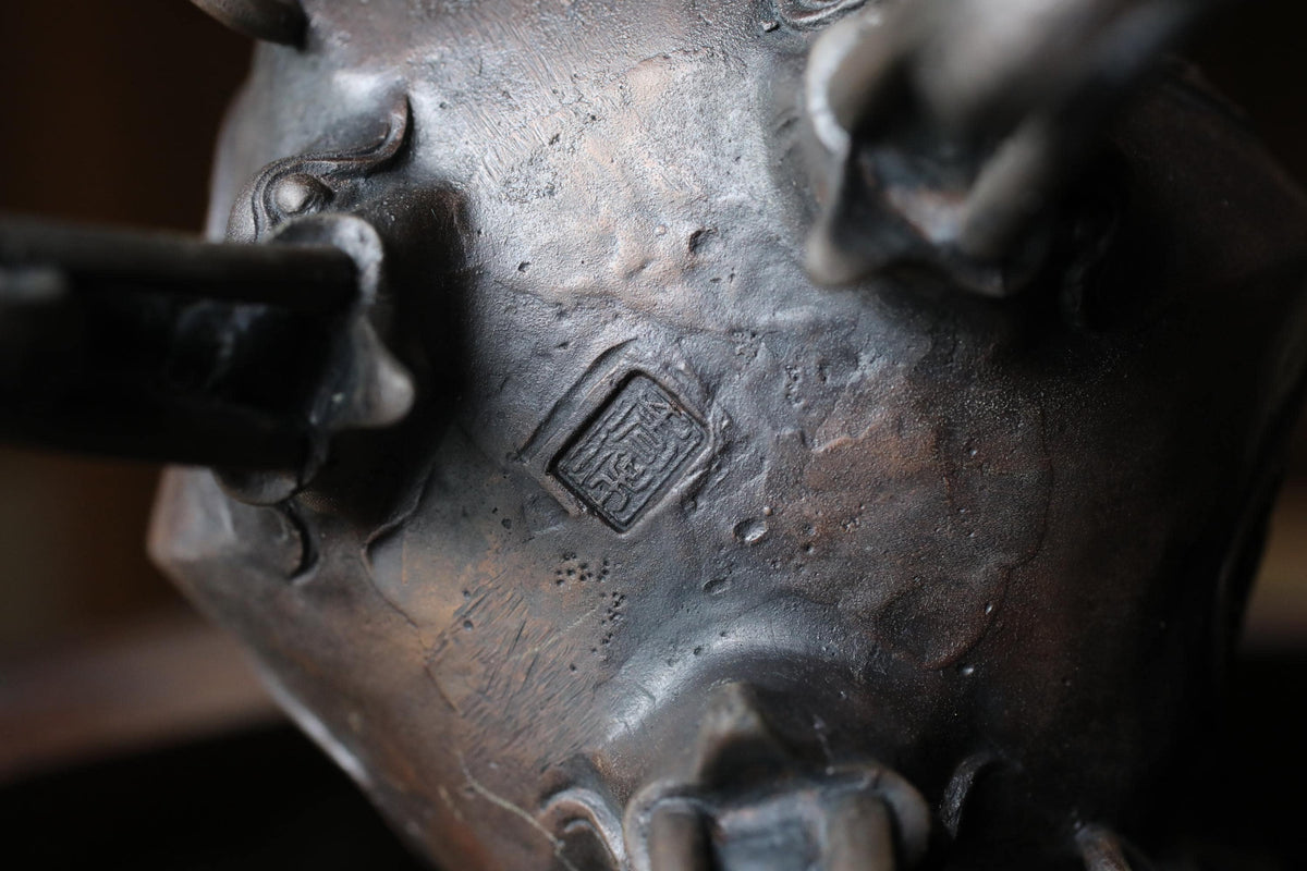 A close-up view of a metal object, possibly a sculpture or a piece of art, with a distinctive marking or symbol on its surface.