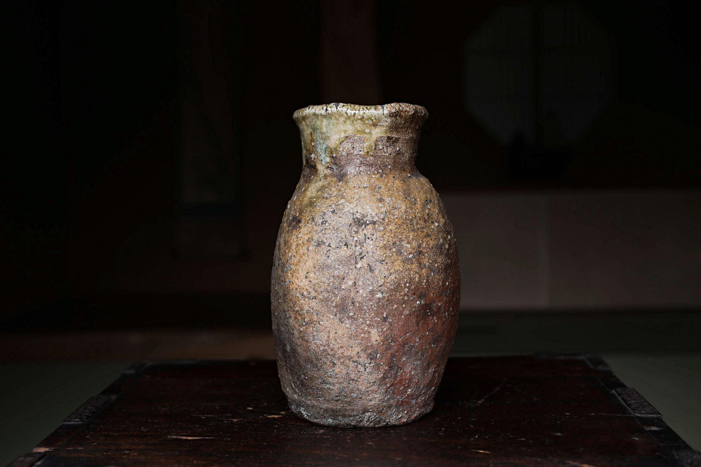 An old, weathered vase sits on a dark wooden surface, its surface showing signs of age and use.
